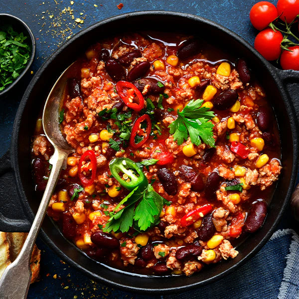 Frisches Chili con Carne in einer schwarzen Pfanne mit roten Bohnen, Mais, Paprika und frischen Kräutern