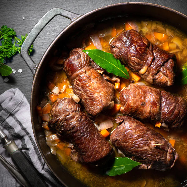 Rinderrouladen in einem schwarzen Topf, serviert mit Gemüse in Bratensauce