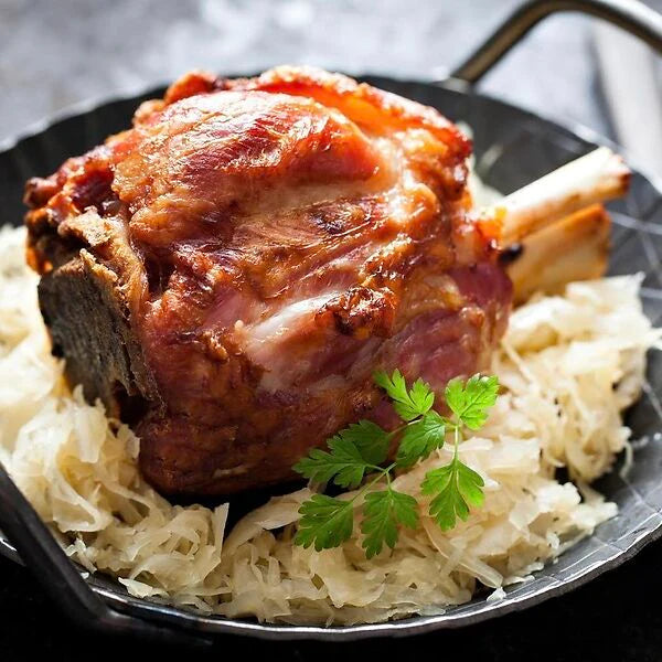 Schweinehaxe vorgegart, serviert auf einem Bett aus Sauerkraut und garniert mit frischer Petersilie in einer schwarzen Pfanne