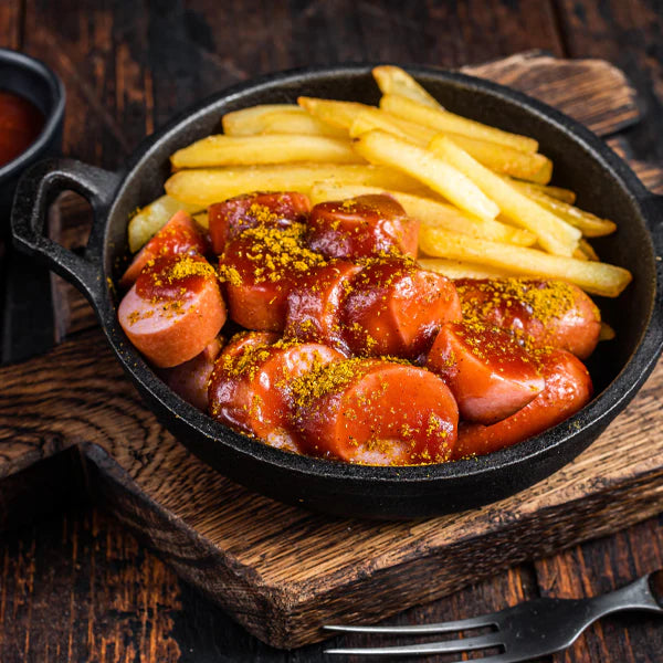 Currywurst mit Pommes in einer schwarzen Pfanne, serviert mit würziger Currysauce und gelben Pommes frites