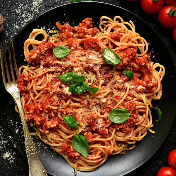 Spaghetti mit Hackfleischsoße nach Bolognese-Art, garniert mit frischen Basilikumblättern und Parmesan auf einem schwarzen Teller