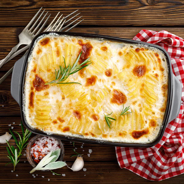 Kartoffelgratin in einer schwarzen Auflaufform, garniert mit frischem Rosmarin, auf einem Holztisch