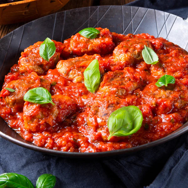 Mini-Frikadellen in Tomatensauce, garniert mit frischen Basilikumblättern in einer schwarzen Pfanne