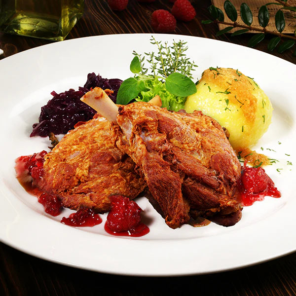 Gebackene Party-Haxen, serviert mit Kartoffelknödel, Rotkohl und Preiselbeersauce auf einem weißen Teller