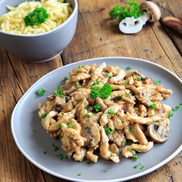 Putengeschnetzeltes in Champignon-Rahmsauce, serviert mit frischer Petersilie auf einem grauen Teller