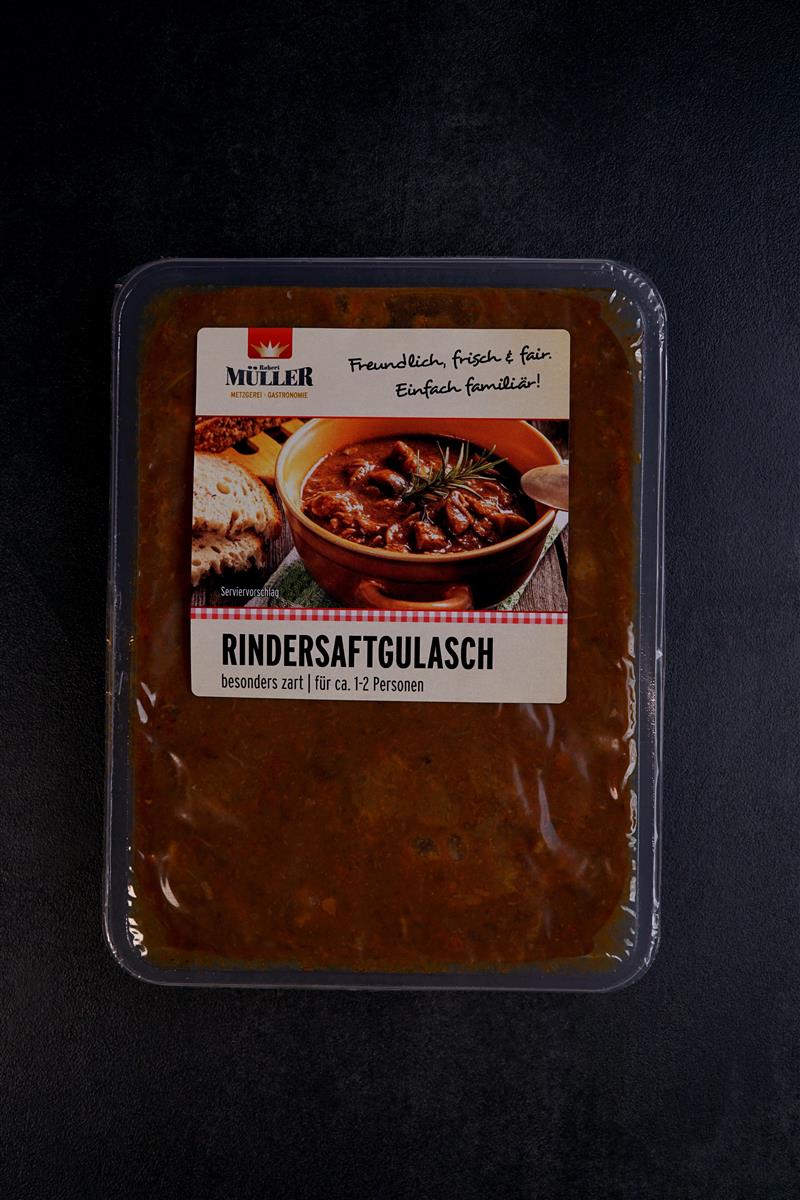Müller Rindersaftgulasch, fertig verpackt in einer reichhaltigen Soße für ca. 1-2 Personen, auf einem schwarzen Tisch